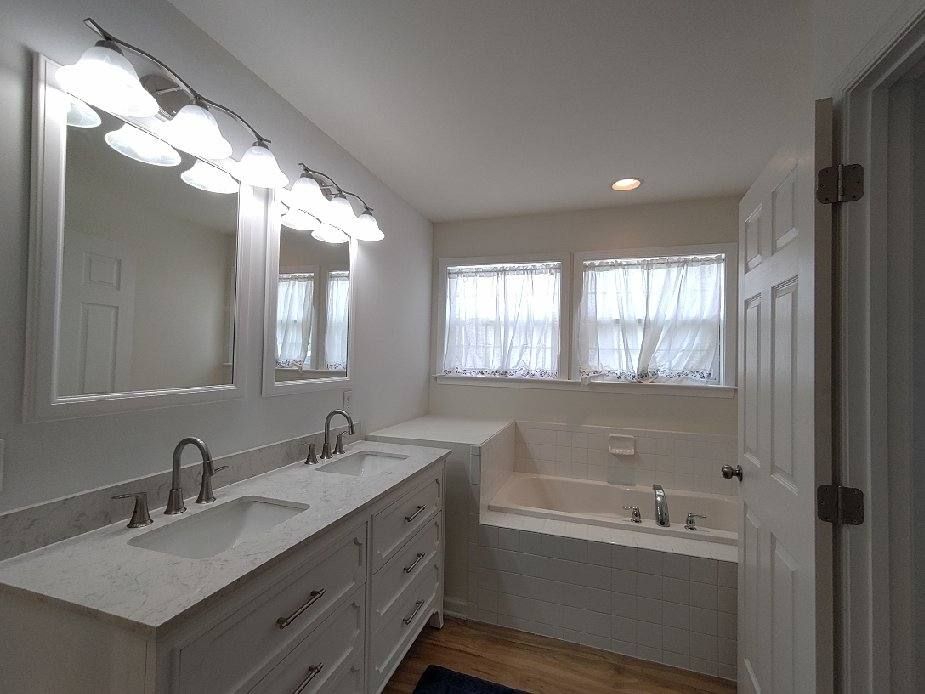 Bathroom with a double vanity, framed mirrors, and a soaking tub under two windows