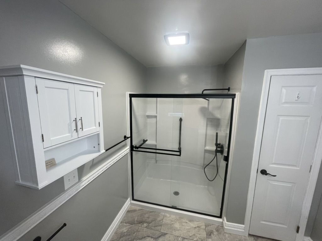 Bathroom with a glass-door walk-in shower, black hardware, and a white wall cabinet