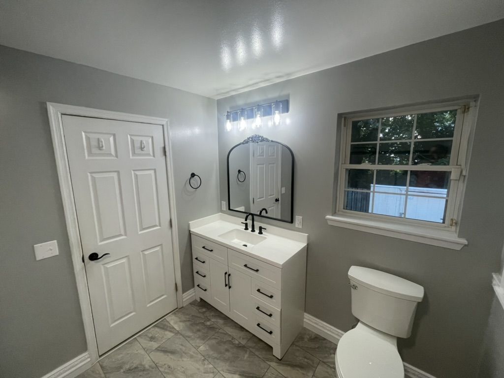 Remodeled bathroom with a white vanity, black fixtures, arched mirror, and gray walls