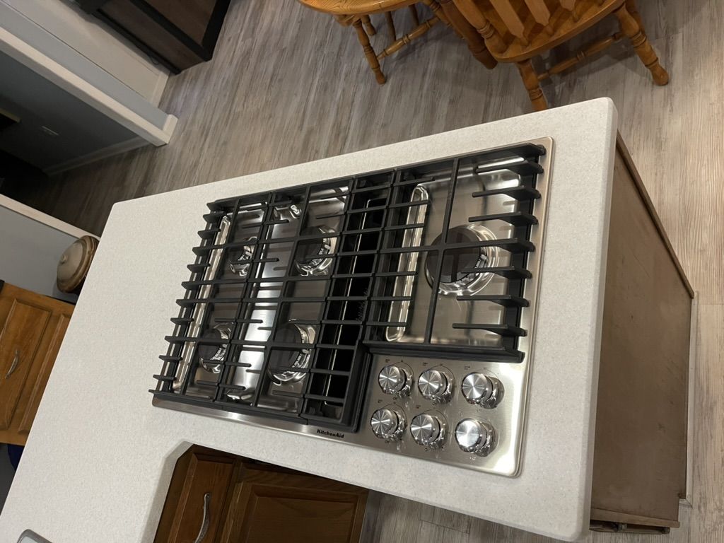 Kitchen island with a gas cooktop set into a white counter over oak cabinets