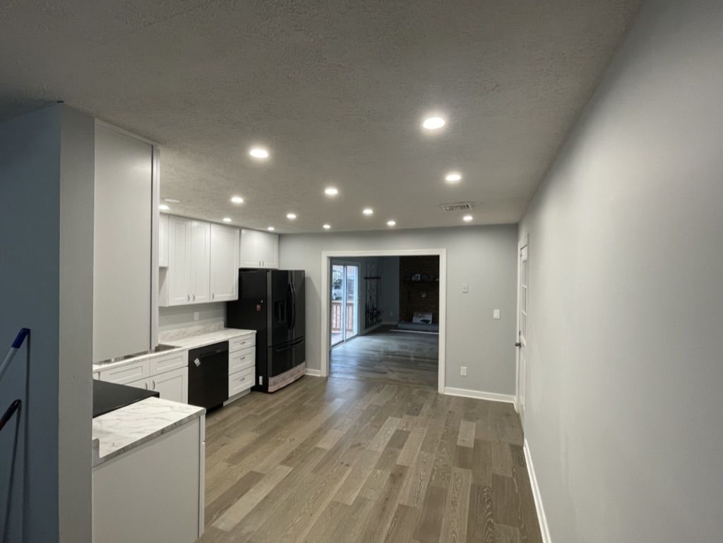 The same view after: white cabinets along the wall, recessed lights, and continuous plank flooring into the family room