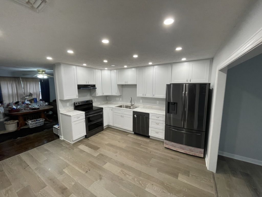 The same kitchen after: white shaker cabinets to the ceiling, recessed lights, and wood-look plank flooring