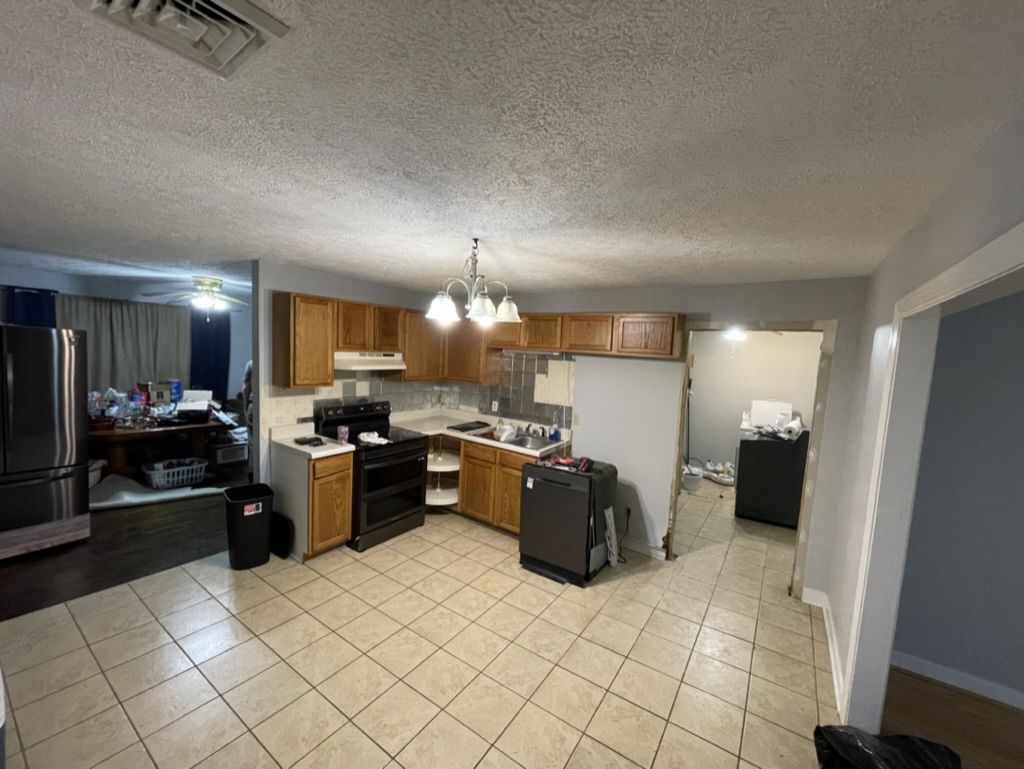 Kitchen before remodeling: oak cabinets, tile floor, hanging chandelier, and a partly removed wall