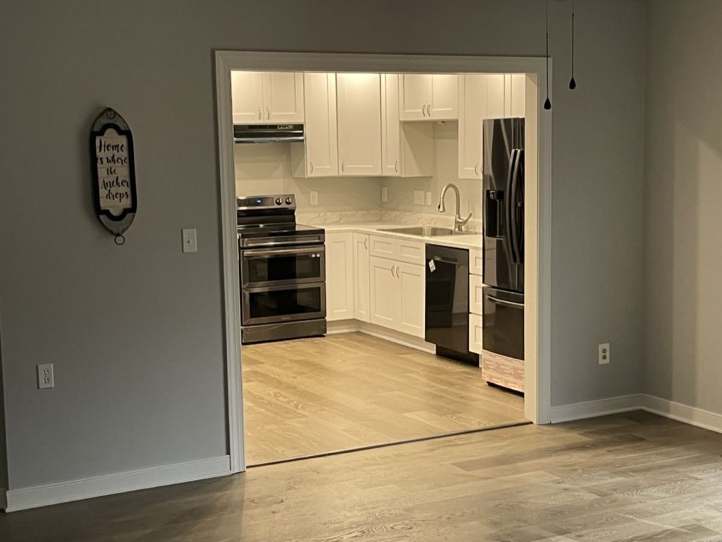 View through a doorway into a white kitchen with stainless range and plank flooring
